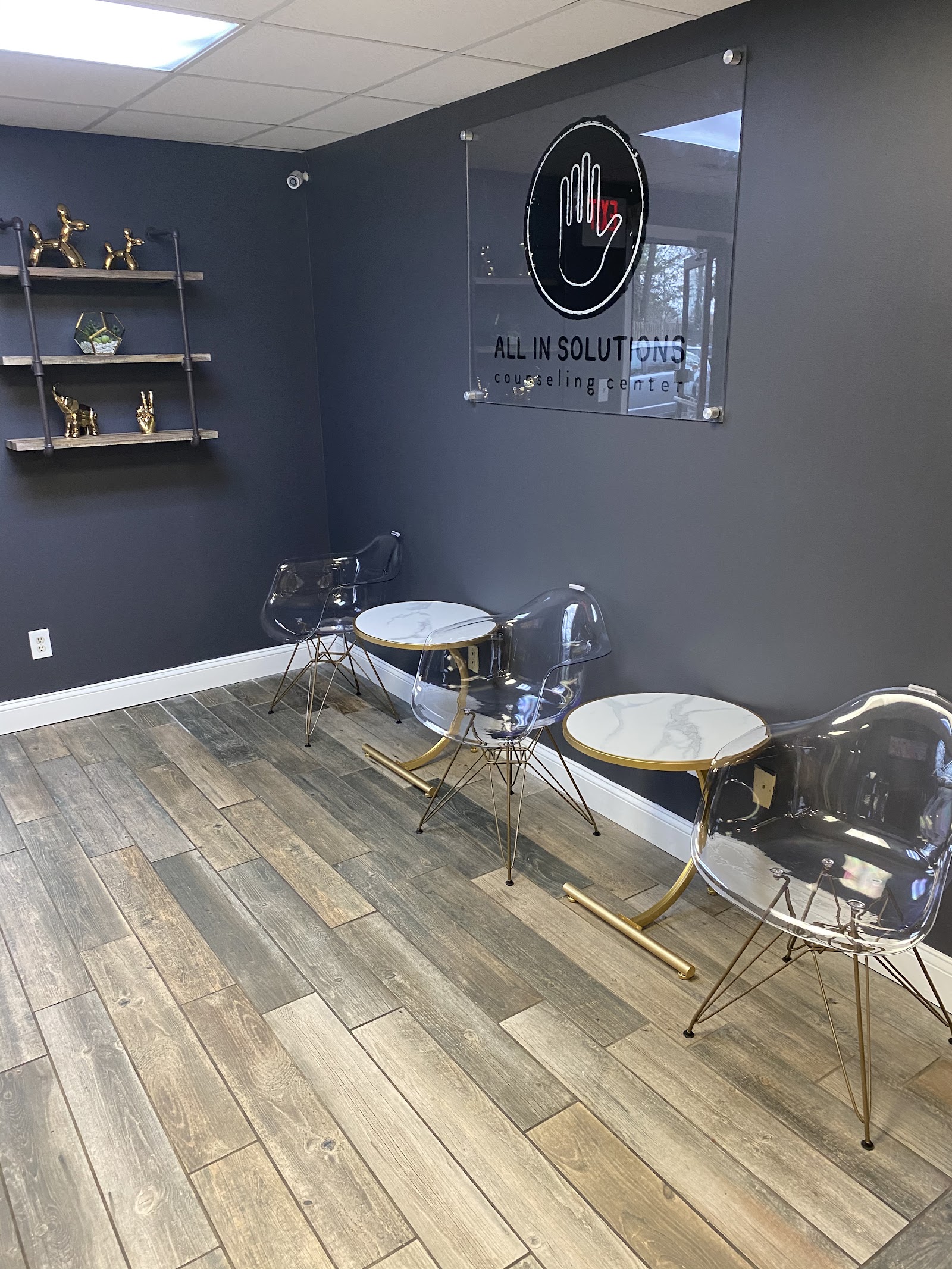 Interior therapy space with dark blue walls, modern seating with gold accents, facility logo, decorative shelving, and wood flooring