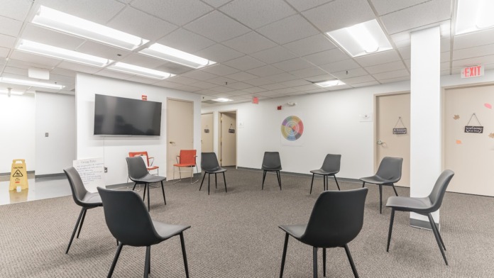 Interior spacious room with multiple black chairs arranged in circle, wall-mounted TV, and motivational wall decor