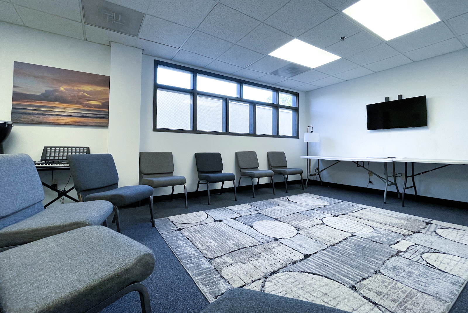 Interior therapy room with comfortable seating, natural lighting, artwork on walls, and entertainment equipment including keyboard and television