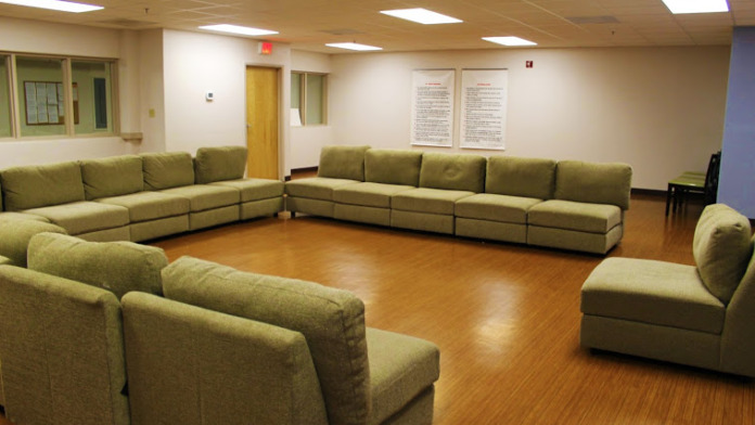 Interior community lounge with modular sectional seating in green and beige, wooden accent elements, and interior signage on walls