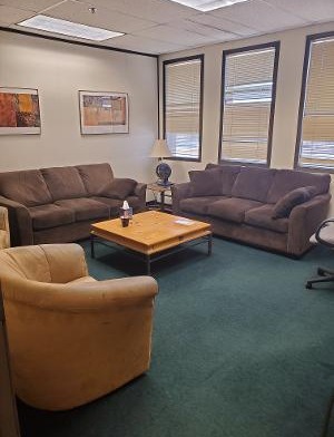 Interior lounge space with multiple upholstered chairs, coffee table with magazines, decorative artwork on walls, and natural lighting from windows