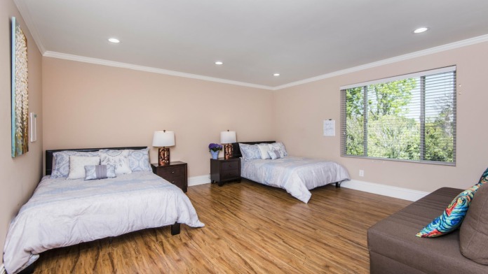Interior bedroom with two beds, hardwood floors, peach walls, large window providing natural light, and furnishings
