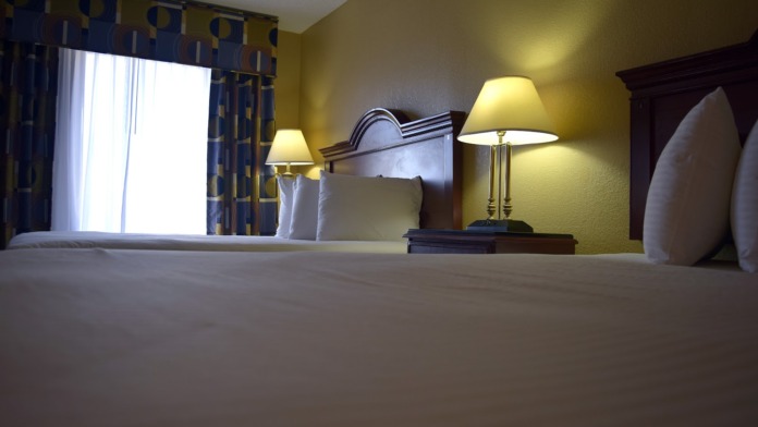 Interior bedroom featuring bed with headboard, table lamps, patterned curtains, and large windows