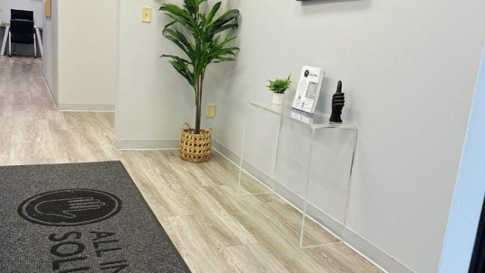Interior hallway with matted entrance flooring, facility branding signage, potted plant, and clean clinical design