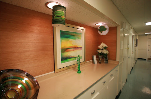 Interior hallway with wood-paneled walls, colorful artwork on walls, flowers in vase, and ceiling light fixtures