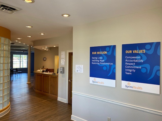 Interior hallway showing wooden flooring, mission and values wall posters with facility branding, reception area in background