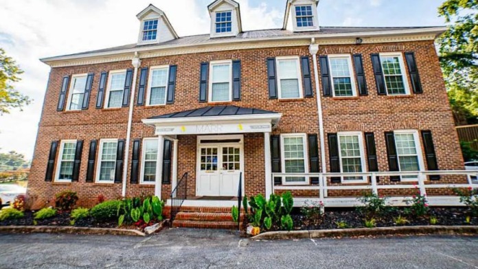 Exterior front of two-story brick building with white trim, multiple windows with shutters, and landscaped entrance with brick pathway