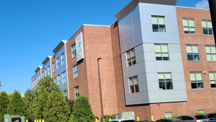 Multi-story brick and modern facade hospital building with parking lot containing multiple vehicles
