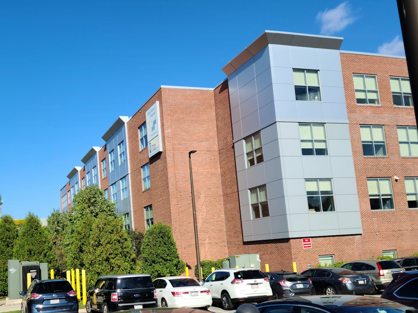 Multi-story brick and modern facade hospital building with parking lot containing multiple vehicles