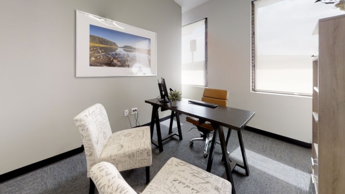 Interior office space with desk, computer equipment, framed landscape artwork, and natural window lighting