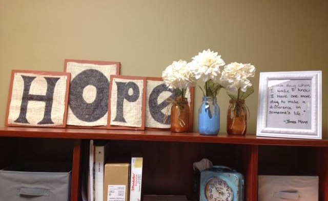 Interior shelf with HOPE wooden letters, flowers in vases, books, and framed motivational quote for facility decor