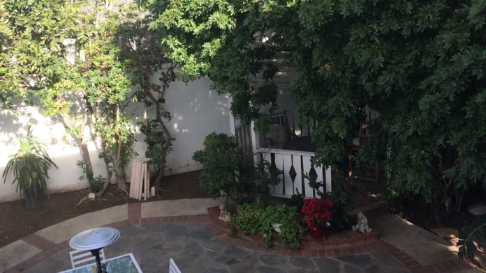 Elevated courtyard view showing brick paving, flowering plants, dining furniture, and ivy-covered facility walls