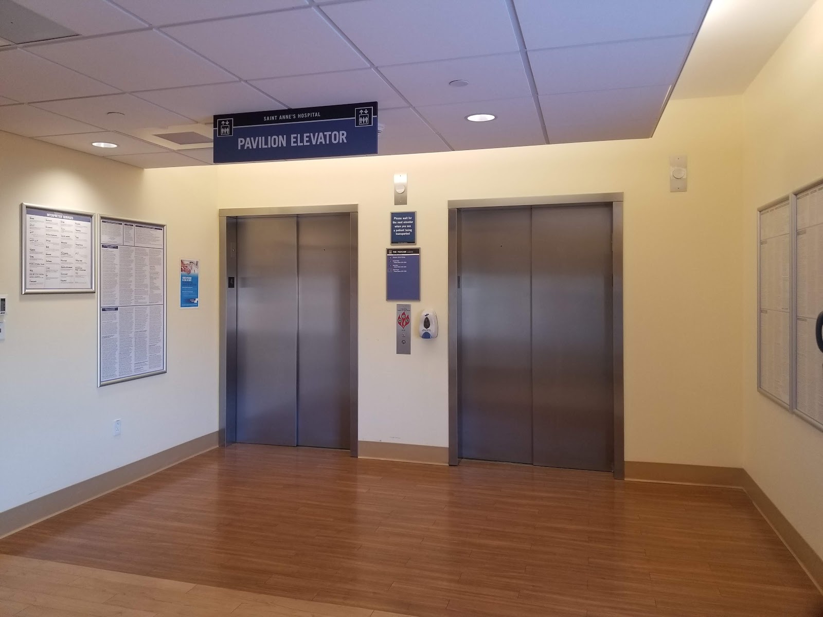 Interior elevator lobby with two elevator doors, signage, information boards, and wood flooring