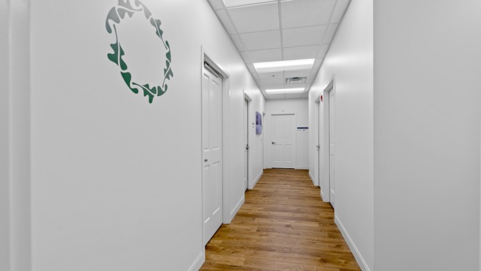 Interior hallway with white doors, decorative facility logo wall decal, wood flooring, and modern ceiling