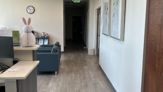 Interior hallway with white and gray walls, recessed lighting, exit sign, framed artwork, and closed doors