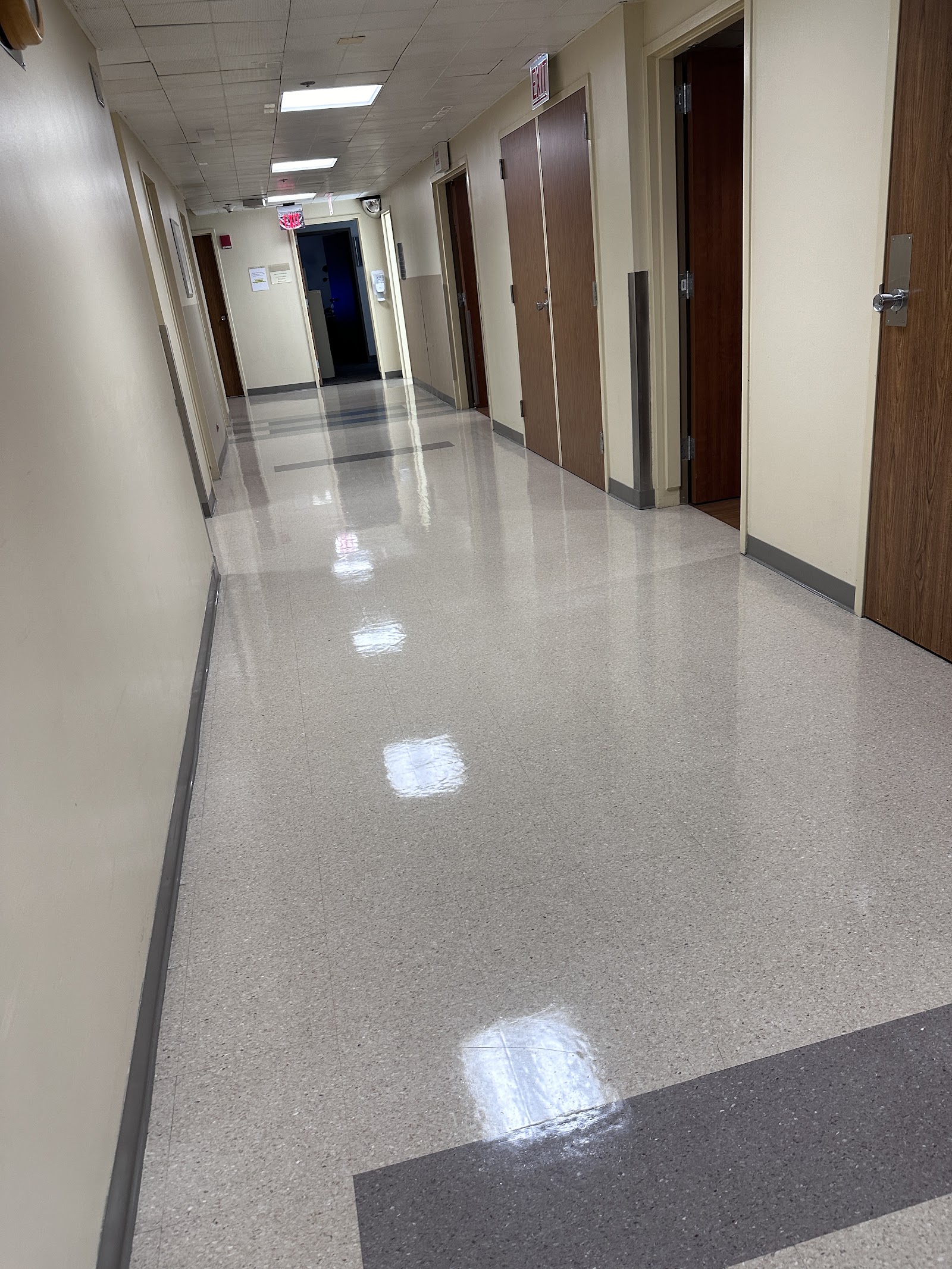 Interior clinical hallway with beige walls, multiple dark wood doors for patient rooms, and polished floors
