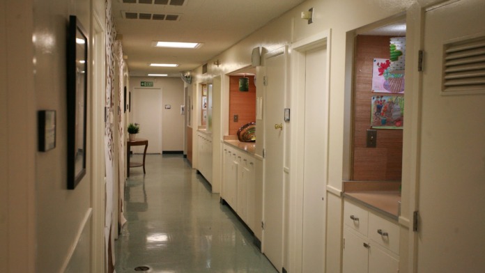 Interior hallway showing multiple patient room doors, white walls, medical signage, and emergency exit