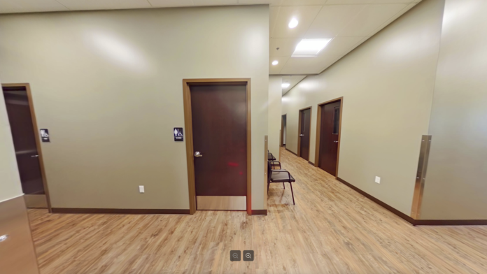 Interior hallway with multiple brown doors, cream walls, wood trim, and institutional lighting throughout