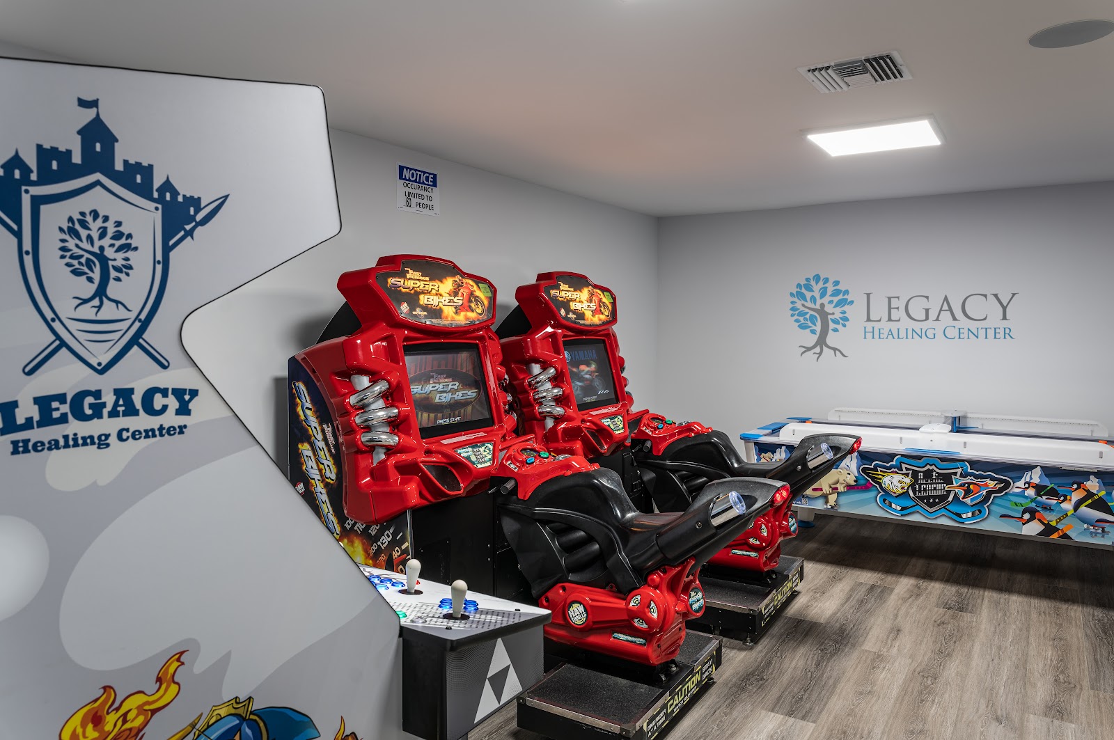 Interior recreation space with red racing arcade game cabinets and blue racetrack flooring with Legacy Healing Center logo on wall