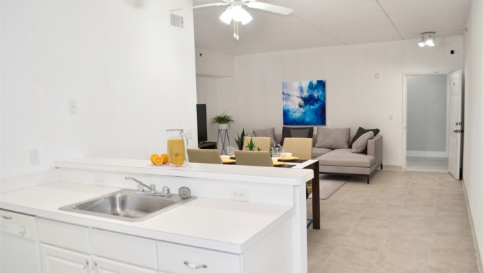 Interior community space with white kitchen area, sink, seating area with gray sofa, and decorative artwork on wall