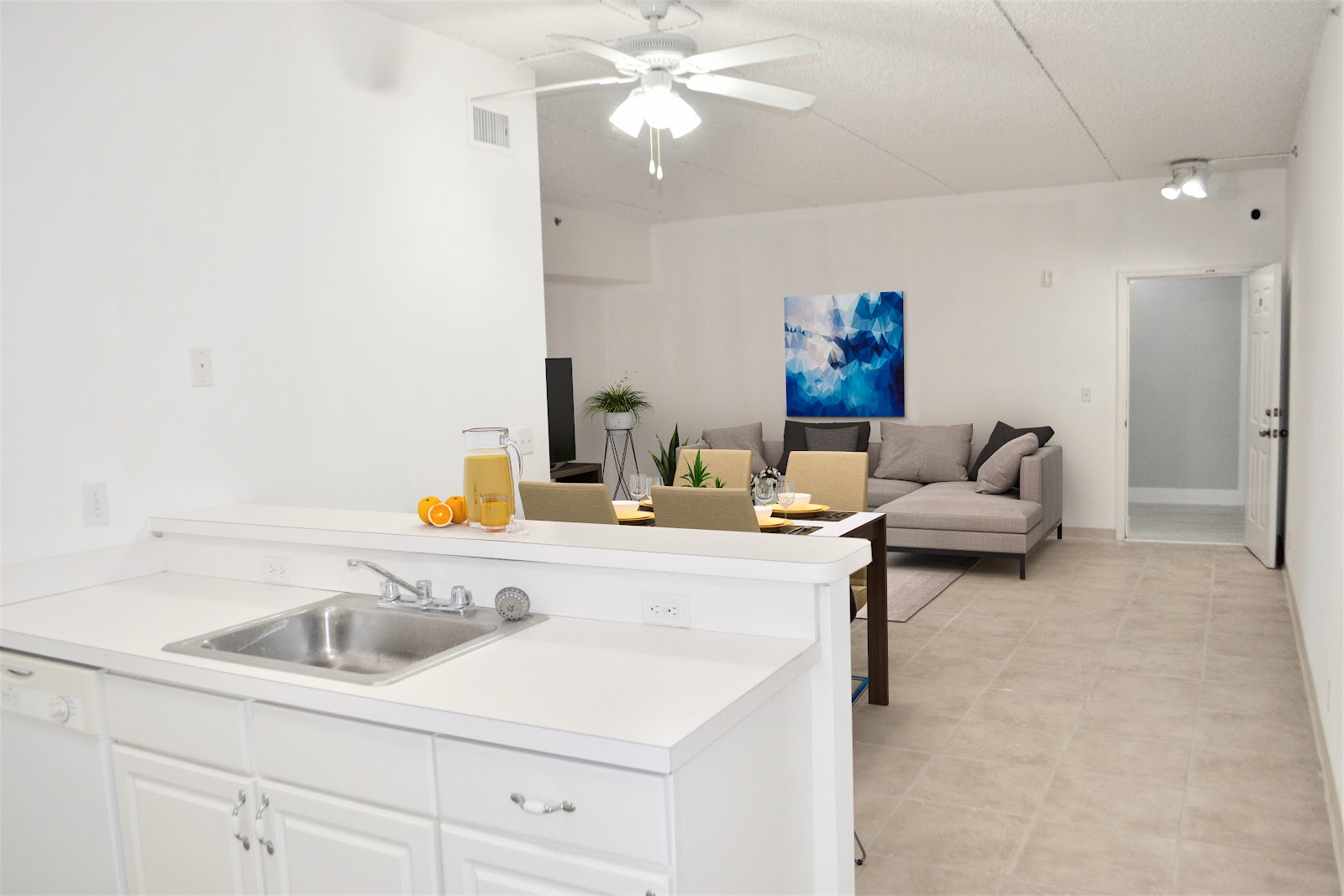 Interior community space with white kitchen area, sink, seating area with gray sofa, and decorative artwork on wall