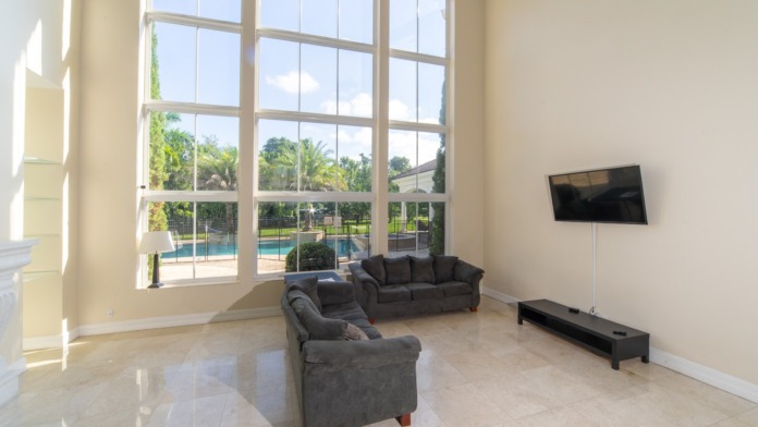 Interior lounge area with oversized windows overlooking pool, comfortable seating, TV, and bright natural lighting