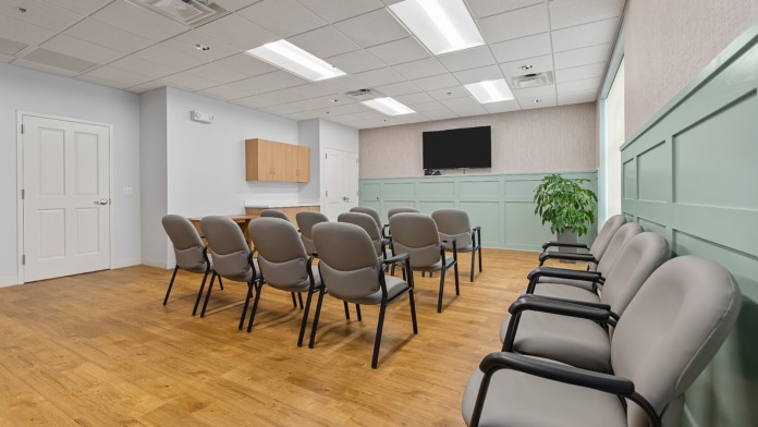 Interior large multipurpose room with arranged gray seating, green and white wall paneling, large TV monitor, and wooden flooring