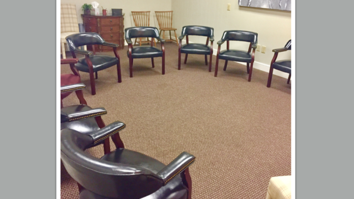Interior group therapy space with multiple black leather chairs arranged in circle, wood tables, and framed wall artwork