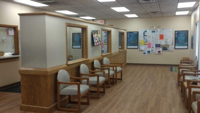 Interior reception area with wood counter dividers, multiple seating areas, information boards, and ceiling lighting fixtures.