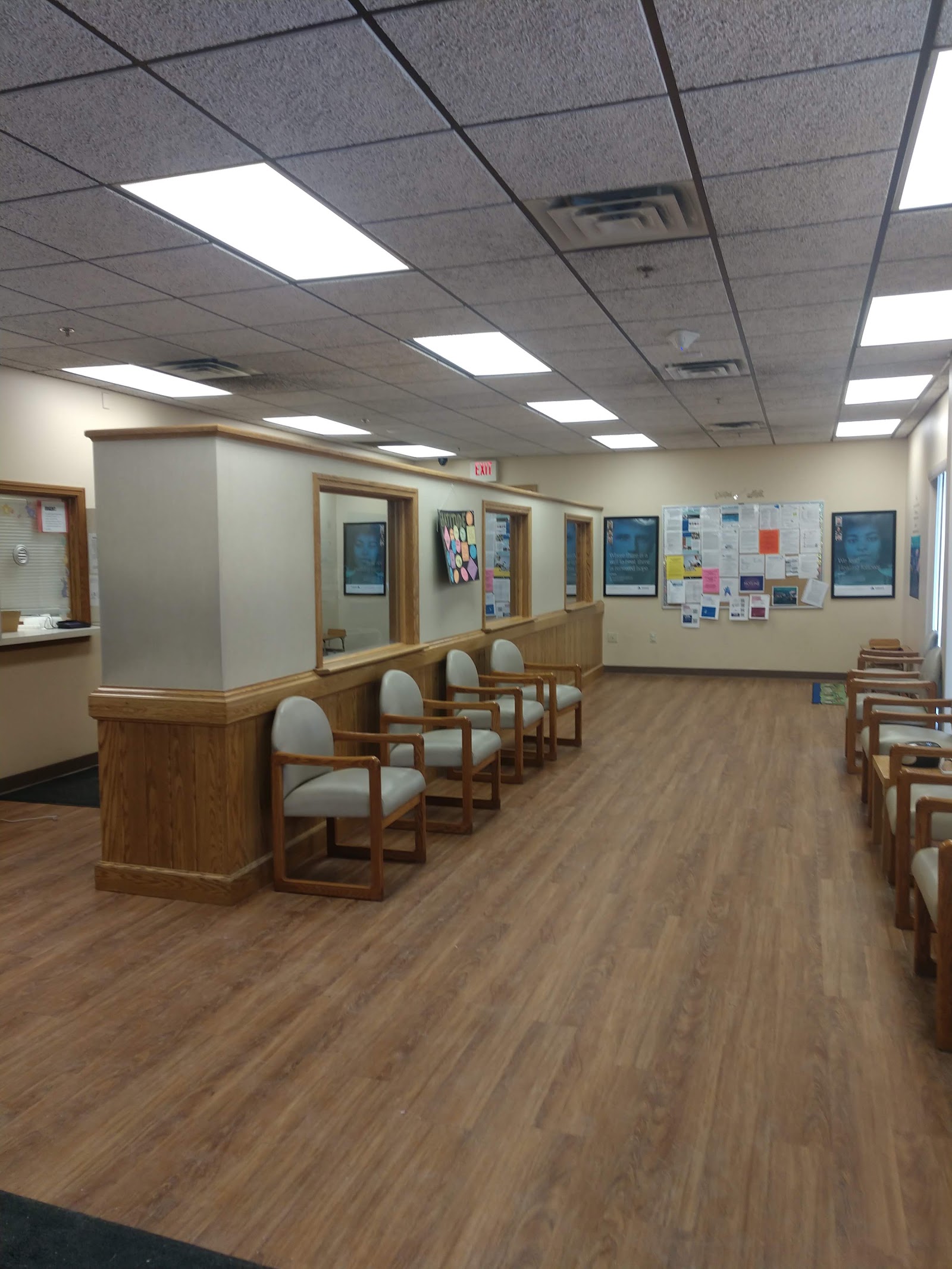 Interior reception area with wood counter dividers, multiple seating areas, information boards, and ceiling lighting fixtures.