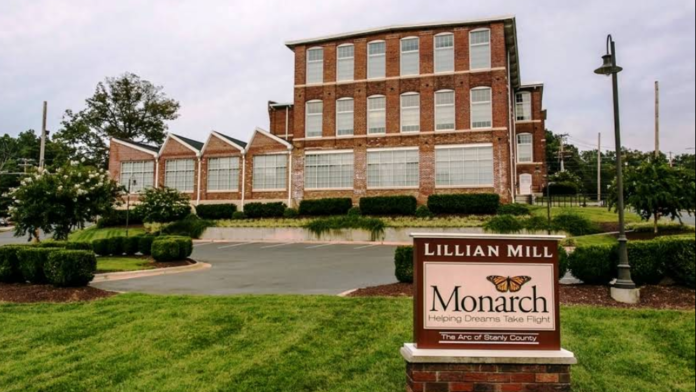 Exterior view of large red brick Monarch Albemarle facility with Lillian Mill signage, green landscaping, and multiple windows