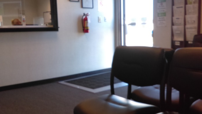 Interior lobby space with reception desk, seating chairs, exit signage, and entry door with natural light
