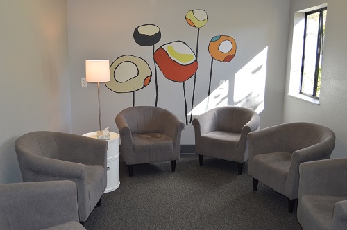 Interior lounge with gray upholstered chairs, decorative colorful floor lamps with abstract shapes, natural window lighting