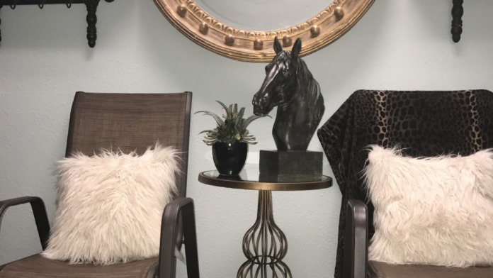 Interior sitting area with upholstered chairs, decorative mirror, plants, clock, and wall shelving