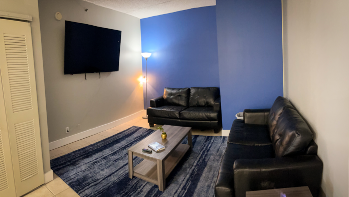 Interior recreation room with black leather sofa, television on wall, blue accent wall, and casual seating