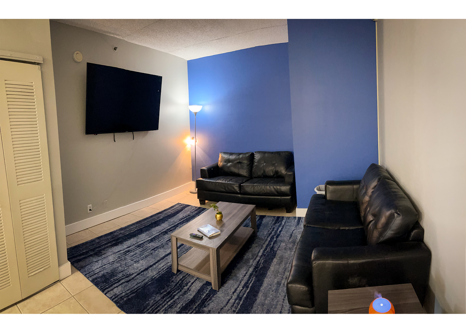 Interior recreation room with black leather sofa, television on wall, blue accent wall, and casual seating