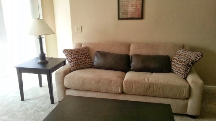 Interior common area with beige sofa, black coffee table, side table with lamp, and motivational wall decor