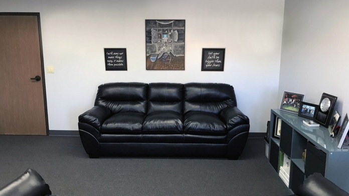 Interior common room with black leather seating, motivational plaques, framed photos on shelves, and additional seating options