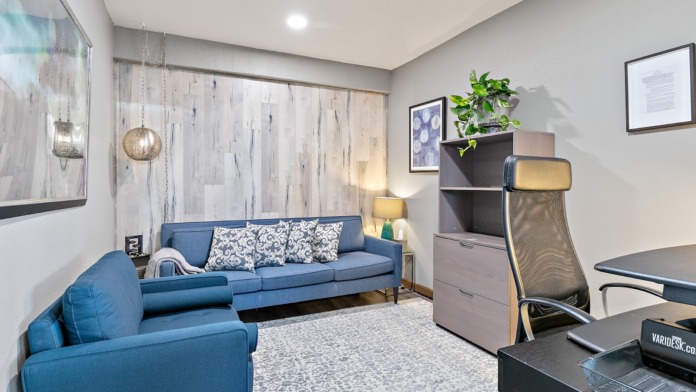 Interior lounge space with blue sofa, accent chairs, large windows with decorative panels, and modern furnishings