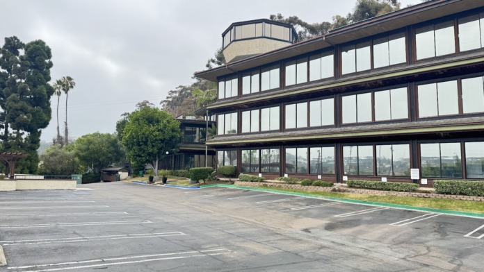 Exterior of modern three-story treatment facility with curved architectural elements, expansive glazing, and parking area.