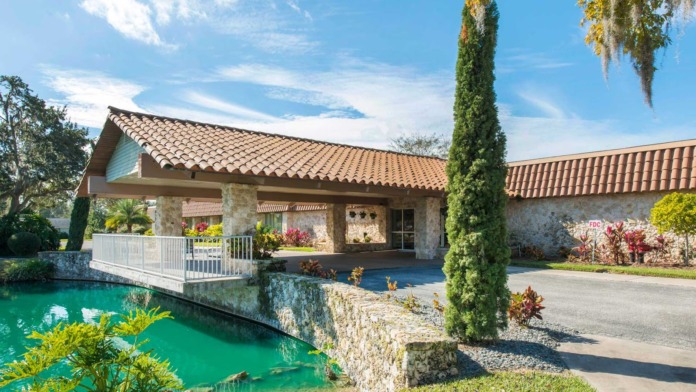 Exterior view of main facility building with stone and tile architecture, pond with water feature, landscaping, and cypress trees