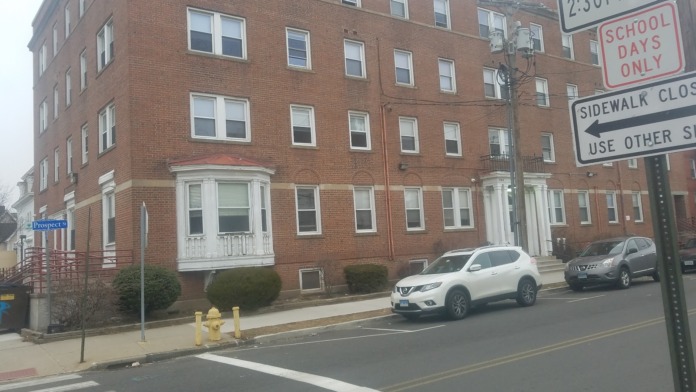 Exterior view of New Prospects brick building with front entrance, parked vehicles, and street signage on Prospect Street
