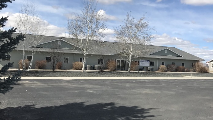 Exterior view of single-story tan and gray medical facility building with wide windows and glass doors visible from parking area
