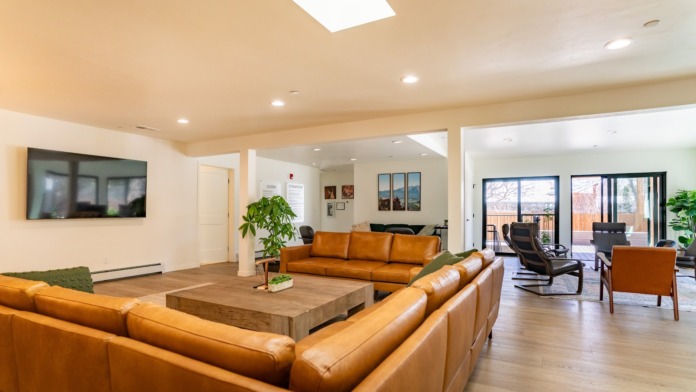 Interior common area with multiple orange leather sofas, wooden coffee table, large windows with mountain views, and television