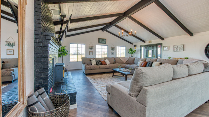 Interior lounge area featuring exposed beam ceiling, brick fireplace, multiple seating areas, and natural light