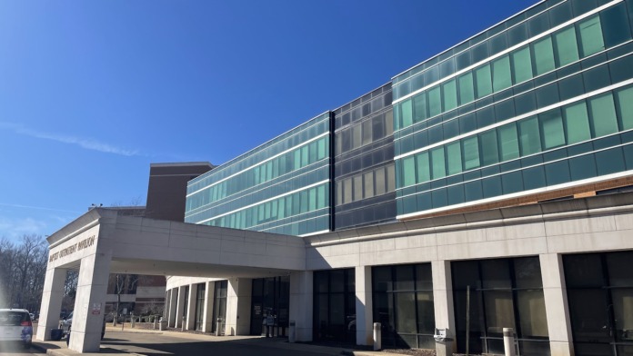 Exterior ground-level view of medical facility entrance with glass doors, modern architectural design, and multi-story glass and metal facade.