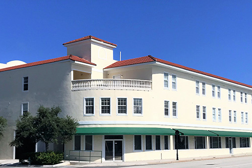 Exterior view of treatment center main entrance with cream and green awning, palm trees, and landscaping
