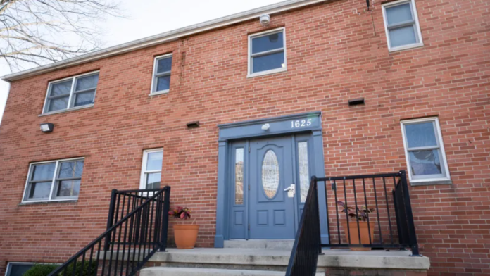 Exterior of two-story red brick building showing blue double doors, entry steps with railings, and address marker 1625