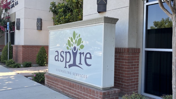 Exterior front facade of treatment facility showing aspire Counseling Services signage with brick base and flowering landscaping