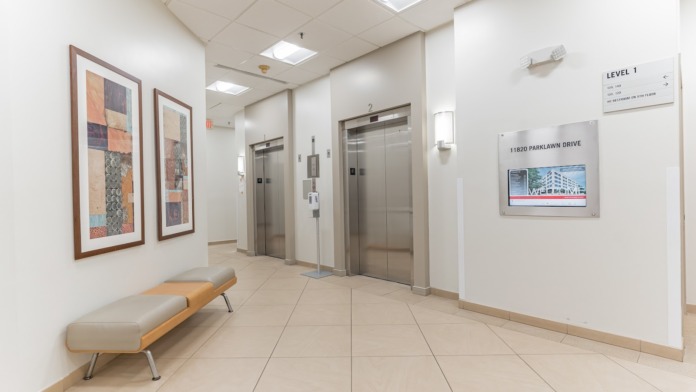 Interior entry foyer with glass doors, entry mat, waiting bench, framed artwork, and directory display